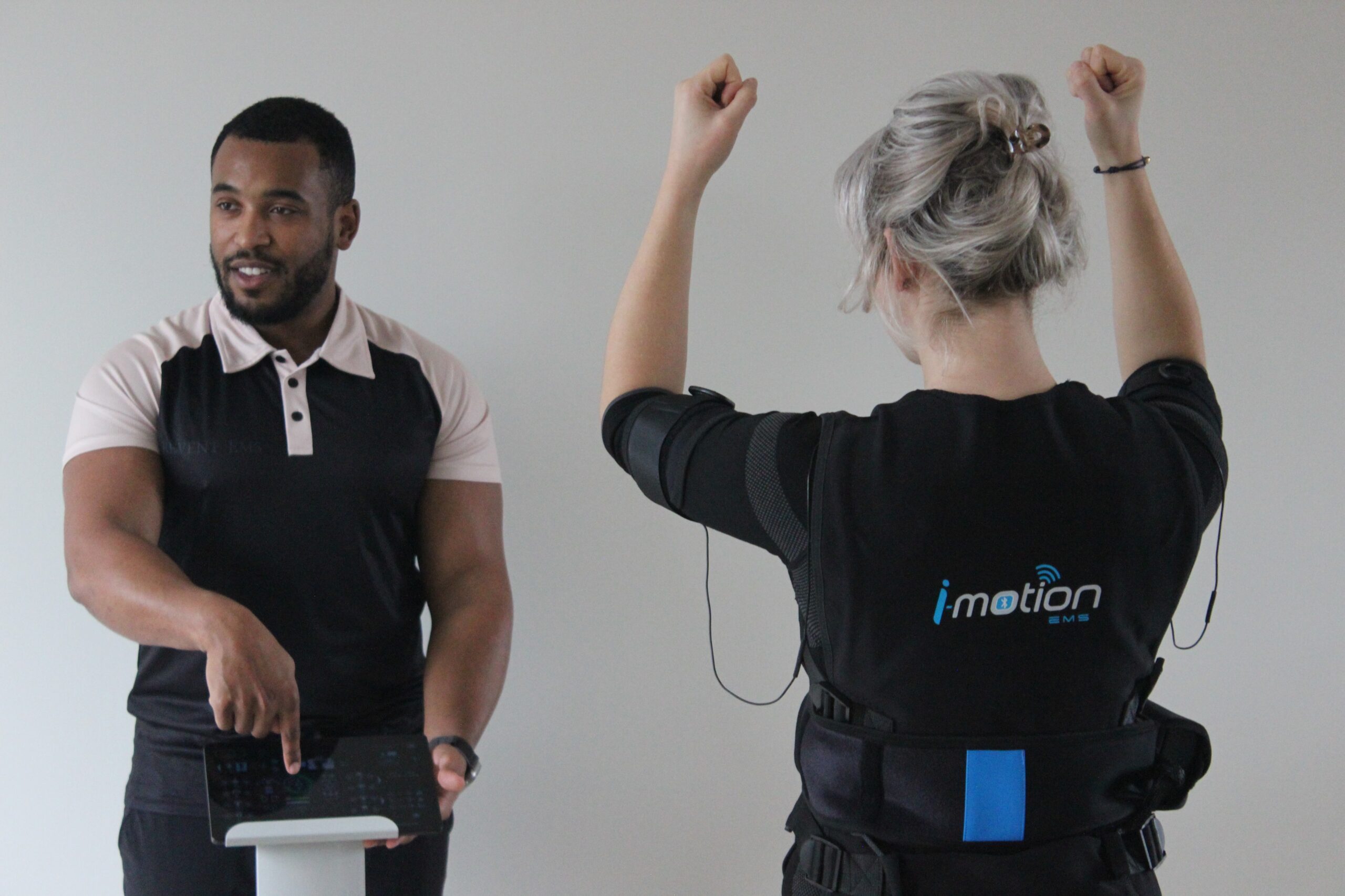 Trainer bij Trevent EMS Amersfoort luxe studio geeft tablet-instructie aan vrouw met EMS-pak, voor fitter worden en meer energie.