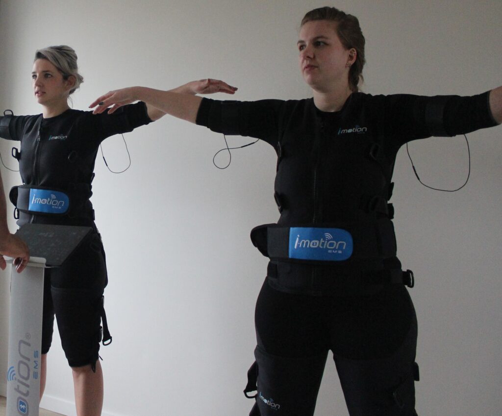 Twee vrouwen sporten met EMS pak met armen wijd tijdens EMS Experience bij Trevent EMS in Amersfoort
