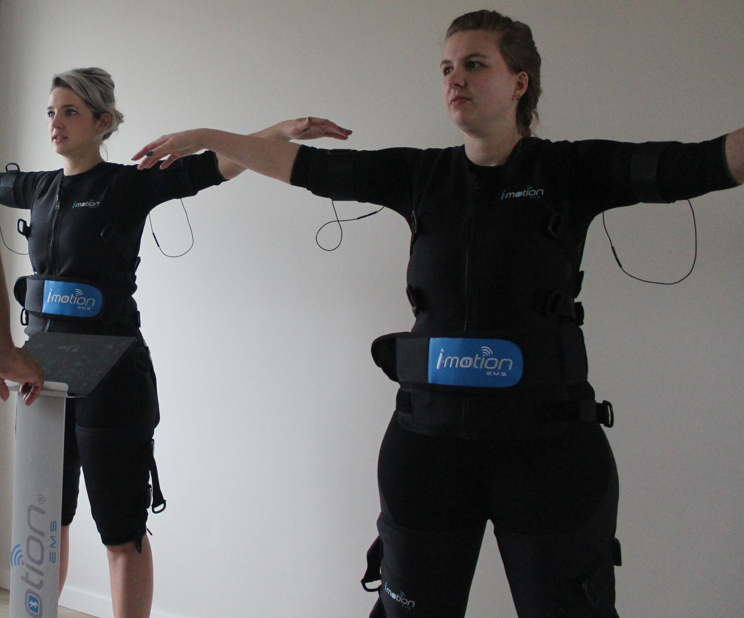 Twee vrouwen sporten met EMS pak met armen wijd tijdens EMS Experience bij Trevent EMS in Amersfoort